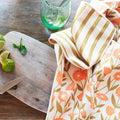 Calendula Flowers Kitchen & Tea Towel displayed on a wooden table with limes and a cocktail glass.