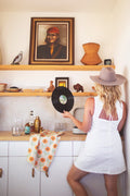Woman holding a vinyl record in a kitchen with California Kitchen & Tea Towel draped over the counter.