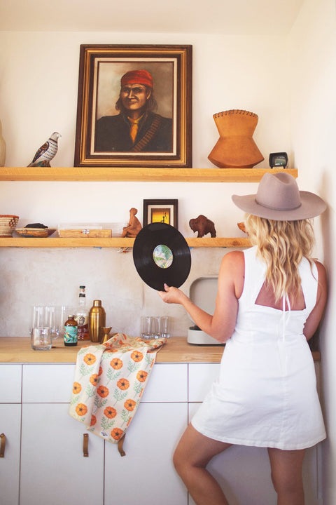 Woman holding a vinyl record in a kitchen with California Kitchen & Tea Towel draped over the counter.