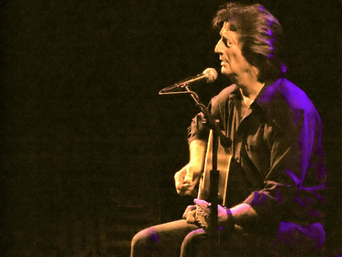 Musician performing on stage with guitar, captured in a vibrant purple light.