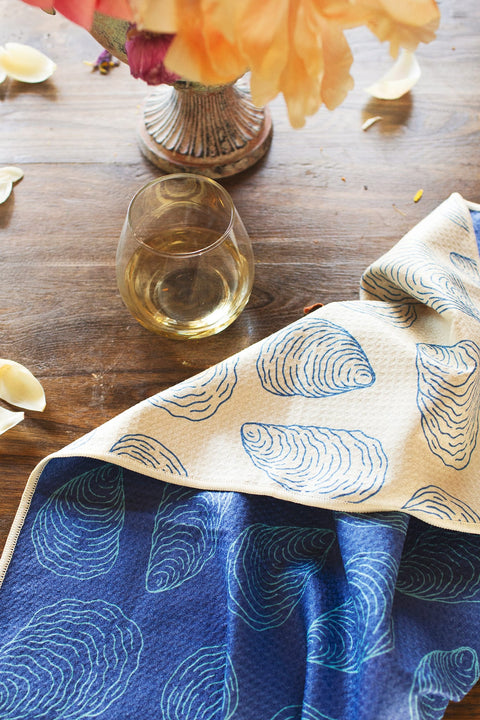 Coastal Oysters Kitchen & Tea Towel displayed on a wooden table with a glass of white wine.