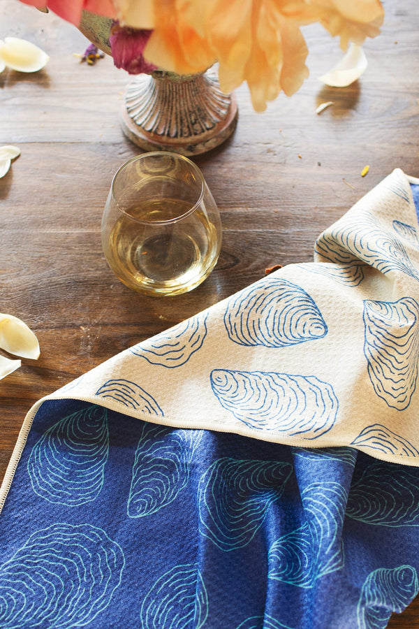Coastal Oysters Kitchen & Tea Towel displayed on a wooden table with a glass of white wine.