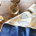 Coastal Oysters Kitchen & Tea Towel displayed on a wooden table with a glass of white wine.