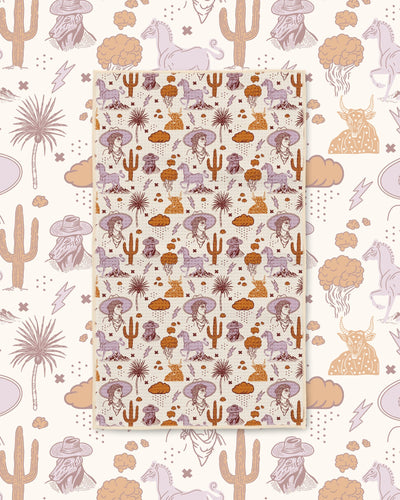 Cosmic Cowgirl Kitchen & Tea Towel with cowgirls, horses, cacti and clouds in purple and orange on cream