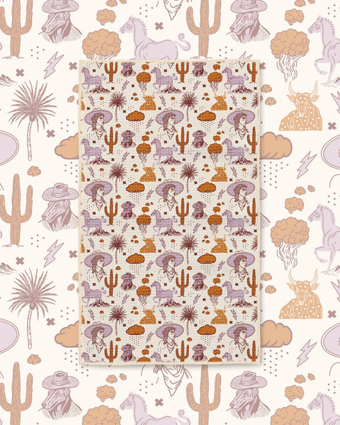 Cosmic Cowgirl Kitchen & Tea Towel with cowgirls, horses, cacti and clouds in purple and orange on cream
