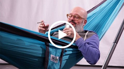 Cozy scene of a man relaxing in a blue Trek Light hammock, enjoying the comfort and serenity with a smile and a sense of contentment.