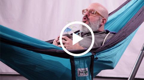 Person relaxing in a blue Trek Light hammock, holding a glass and enjoying a peaceful moment. Perfect for outdoor relaxation.