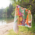 Vibrant Trek Light towel hanging by a serene lake amidst lush greenery, perfect for outdoor adventures.