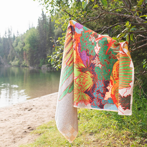 Vibrant Trek Light towel hanging by a serene lake amidst lush greenery, perfect for outdoor adventures.