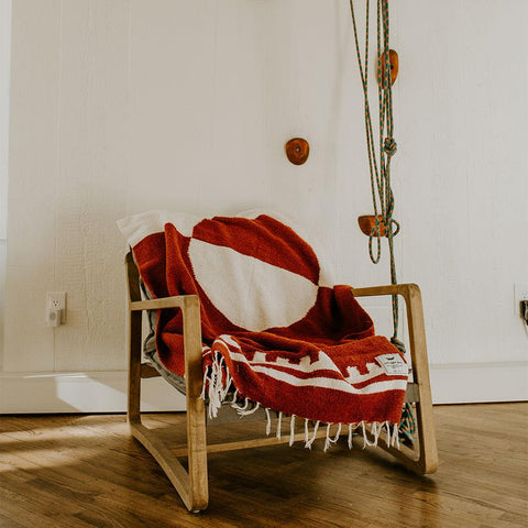 Cozy rust and white Divided Sky Blanket by Trek Light draped over a wooden chair, showcasing its artisan handwoven design and sustainable charm.