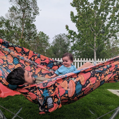 Man and baby enjoying a cozy moment in a Trek Light double hammock with a colorful midnight mushroom print.