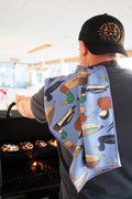 Person using Ducks In A Row Kitchen & Tea Towel while grilling, showcasing vibrant duck designs and practicality.