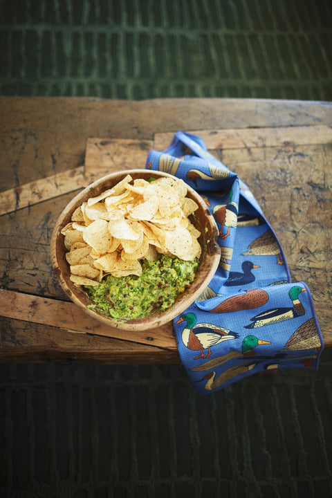 Ducks In A Row Kitchen & Tea Towel next to a bowl of guacamole and tortilla chips on a wooden table.