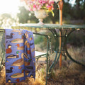 Ducks In A Row Kitchen & Tea Towel draped over a chair next to a table with flowers, showcasing vibrant duck designs.