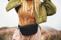 Woman wearing Everyday Fanny Pack (Eclipse) in an outdoor setting, showcasing waterproof design and multiple zippered pockets.
