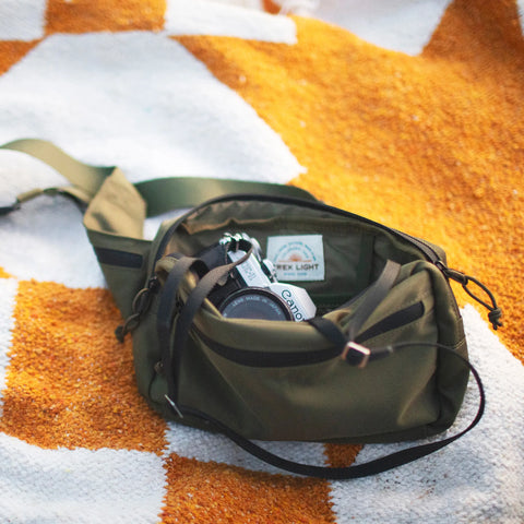 Everyday Fanny Pack (Fern) on a picnic blanket, showcasing its spacious and versatile design with multiple pockets and zippers.