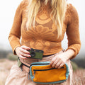 Woman wearing Everyday Fanny Pack (Golden Hour) with camera, showcasing versatile design for travel and daily use.