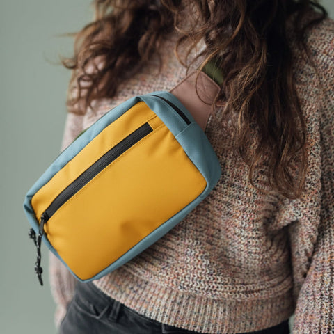 Colorful crossbody bag with blue and yellow panels on person wearing a knitted sweater, showcasing stylish accessory design.