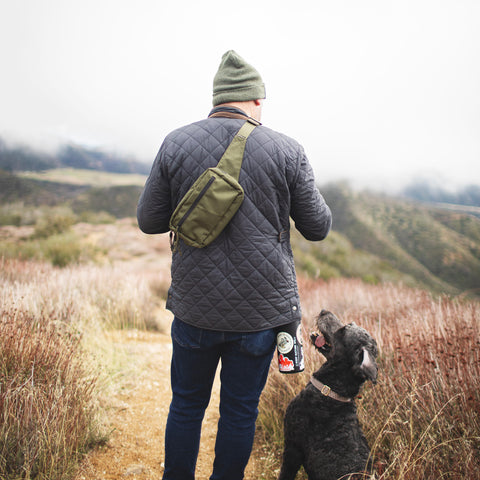 Person hiking with dog wearing Everyday Fanny Pack (Fern) as a crossbody sling, highlighting outdoor versatility and style.