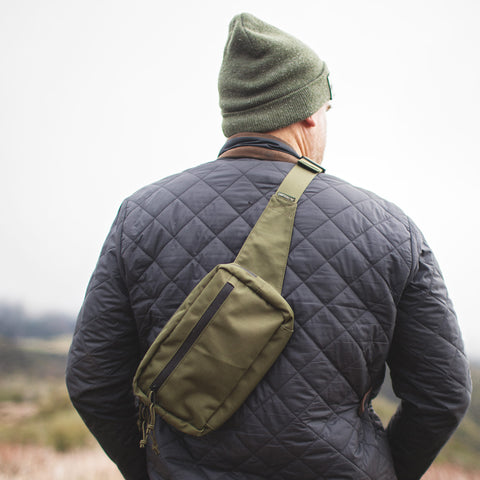 Man wearing Everyday Fanny Pack (Fern) as a crossbody sling, showcasing its versatility in outdoor setting.