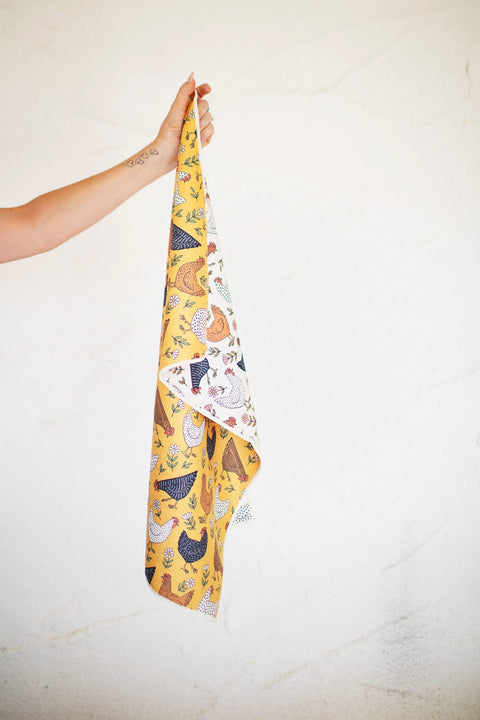 Farmhouse Chicken Kitchen & Tea Towel being held with colorful chicken design on a yellow background.