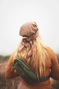 A woman wearing the Everyday Fanny Pack (Fern) in a lush outdoor setting, highlighted by her patterned scarf and hair.