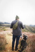 Person hiking with dog wearing Everyday Fanny Pack (Fern) as a crossbody sling, highlighting outdoor versatility and style.