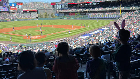 Kids watching a baseball game in a crowded stadium, with lively atmosphere and sunny weather.