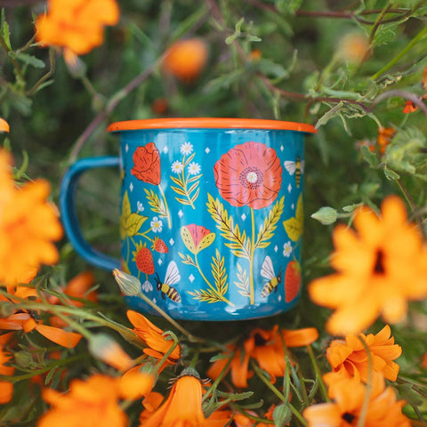 Trek Light 16oz Garden Buzz Enamel Mug amidst vibrant orange flowers, perfect for outdoor adventures.