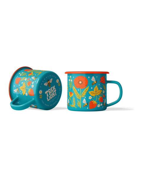 Two Garden Buzz Enamel Mugs in teal with orange rims and bee, poppy and strawberry prints, one tipped on its side, on white