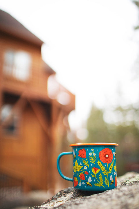 Garden Buzz Enamel Mug 16oz displayed outdoors with colorful floral design on a stone surface.
