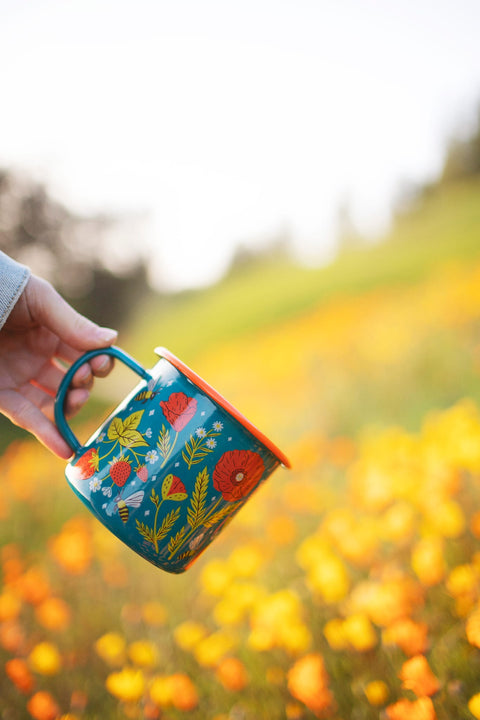 Garden Buzz Enamel Mug 16oz held in hand against a colorful flower background.