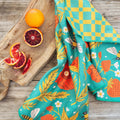 Garden Buzz kitchen and dish towel with vibrant garden design, eco-friendly and super absorbent, displayed with oranges on a wooden board.