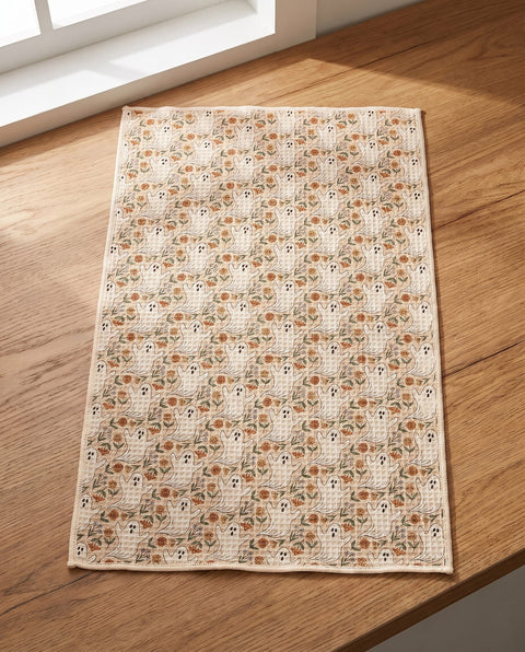 Ghost Garden kitchen tea towel laid flat on a wood counter showing the full cream front print