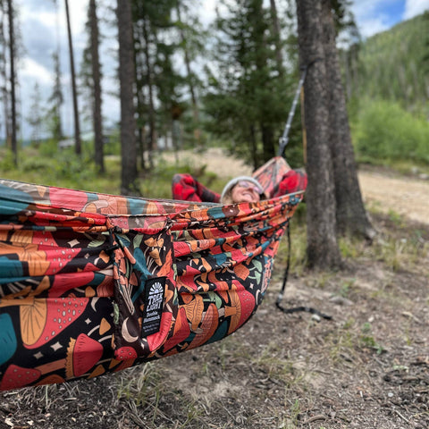 A person relaxing in a Double Hammock & Pro Hanging Straps (Butterfly Dreams Print) in a forest setting.