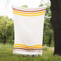 Golden Age Blanket with yellow and brown stripes, handwoven from recycled materials, displayed outdoors.