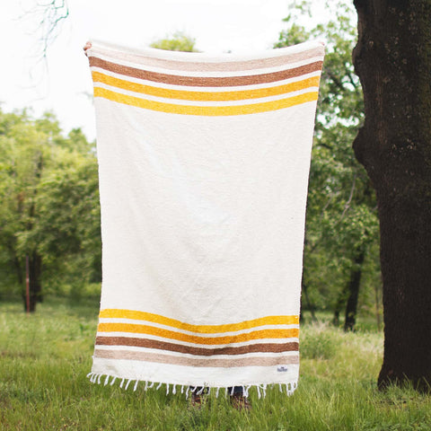 Golden Age Blanket with yellow and brown stripes, handwoven from recycled materials, displayed outdoors.