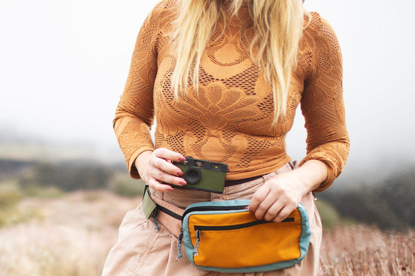 Woman wearing Everyday Fanny Pack (Golden Hour) with camera, showcasing versatile design for travel and daily use.