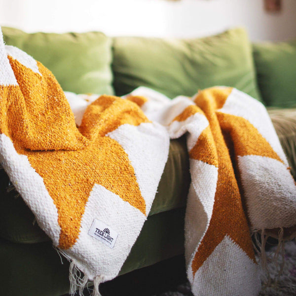 Cozy handwoven Goldie blanket with geometric design, made from recycled clothing materials, draped over a green sofa. By Trek Light.