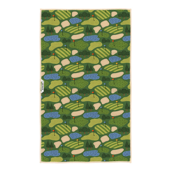 Close-up of Golf Dreams tea towel design showing detailed illustrations of striped fairways, putting greens, trees, and golf holes in vibrant green and yellow tones