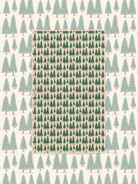 Gondola Winter tea towel laid over a matching cream ski resort pattern of mountains, gondolas, and pines