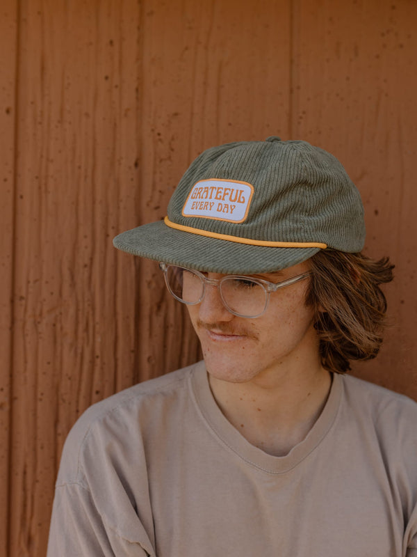 Man wearing Grateful Every Day hat by Trek Light, green corduroy snapback with flat brim, showcasing gratitude style.