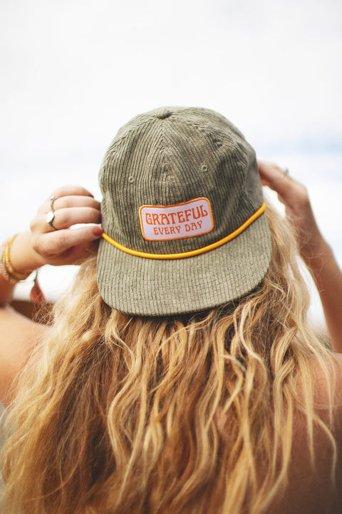 Person wearing Trek Light Grateful Every Day hat with flat brim and corduroy style, perfect for expressing gratitude and style.