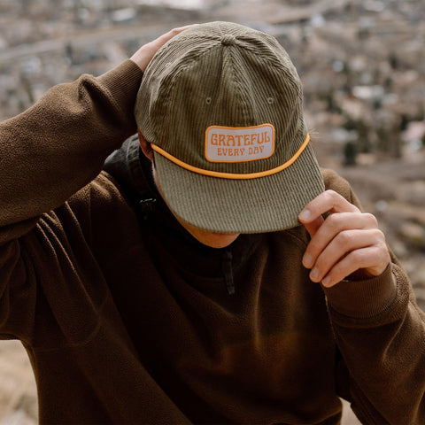 Person wearing Grateful Every Day corduroy snapback hat with Trek Light style in an outdoor setting.