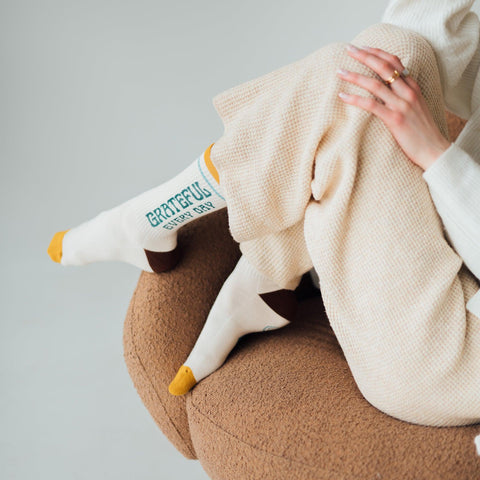 Person relaxing in cozy "Grateful Every Day" socks by Trek Light, showcasing comfort and style on a cushioned chair.