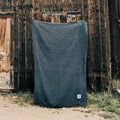 Greyson Blanket: cozy, handwoven, and beautiful, made from recycled materials. A versatile Trek Light companion against rustic wood backdrop.