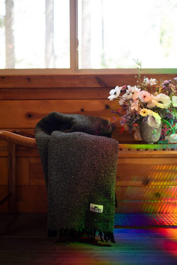 Greyson Blanket draped over a wooden bench near a flower arrangement in a cozy setting.