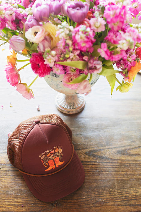 Grow Your Own Way Hat on a wooden table beside a floral arrangement, capturing vibrant colors and unique design.
