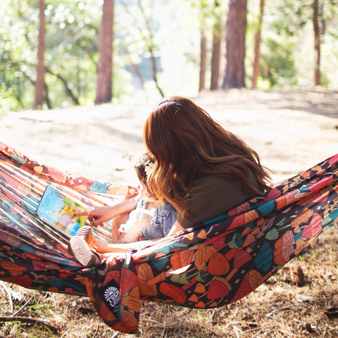 Woman and child enjoying a book in a Double Hammock & Pro Hanging Straps (Midnight Mushroom Print) in the woods.