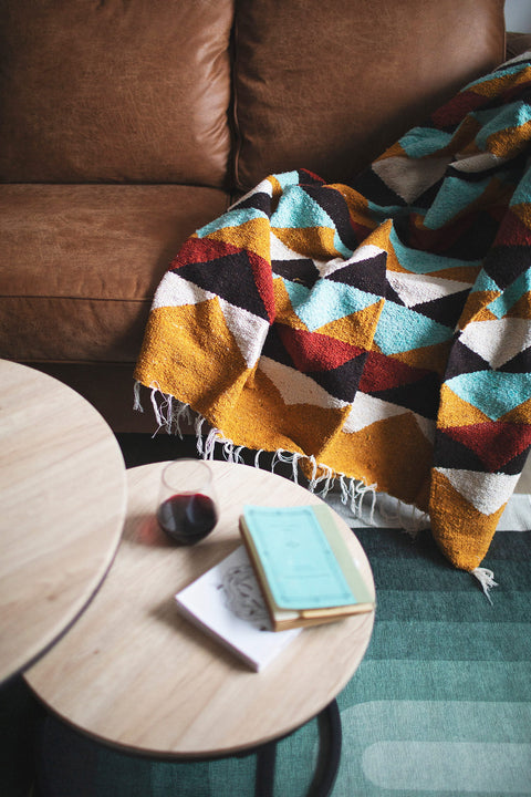 Colorful geometric blanket draped over a brown sofa with wooden tables in a cozy living room setting.